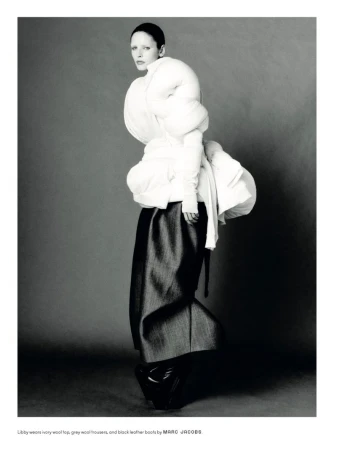 Editorial fashion shot: Woman in avant-garde white top, grey wool trousers, and black leather boots in a studio setting.