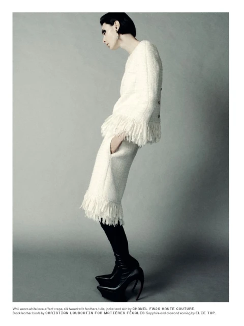 A woman poses in a cream-colored jacket with fringe and matching pants, plus black platform boots against a neutral background.