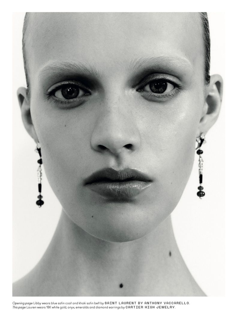 Extreme close-up portrait of a female model wearing long dangling earrings against a plain white background.