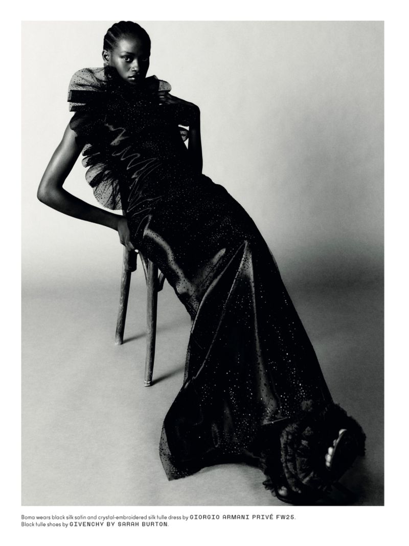 Elegant woman in a black silk dress posing on a wooden chair in a studio setting, showcasing fashion and editorial style.