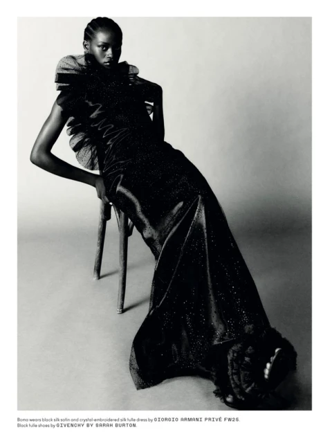 Elegant woman in a black silk dress posing on a wooden chair in a studio setting, showcasing fashion and editorial style.