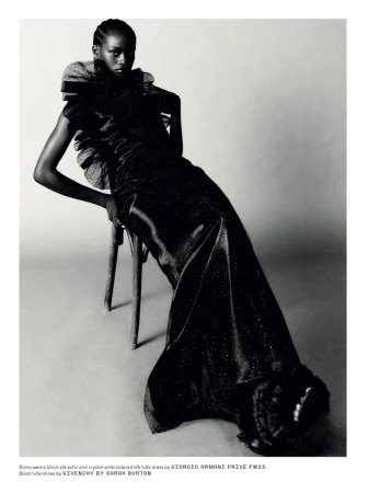 Elegant woman in a black silk dress posing on a wooden chair in a studio setting, showcasing fashion and editorial style.