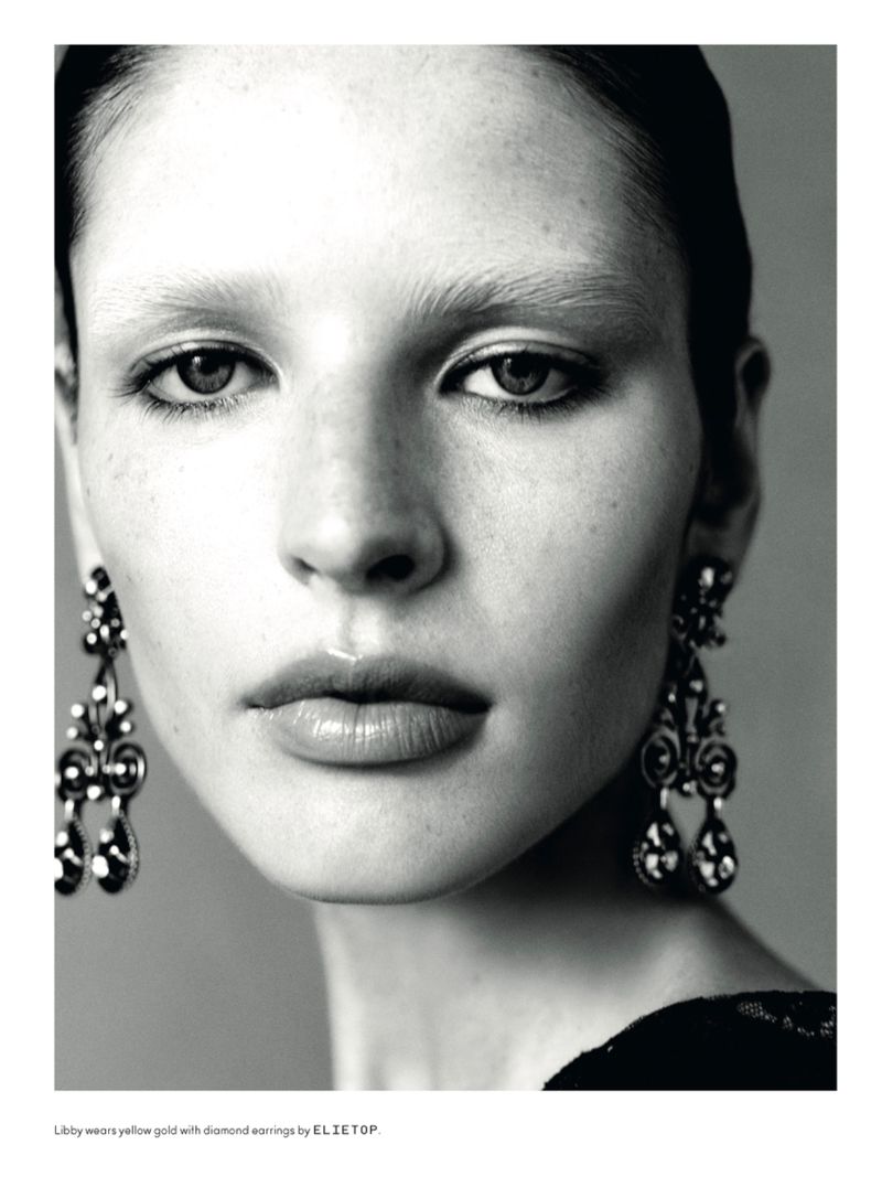 Close-up portrait of a woman wearing ornate dangle earrings and dark eyeliner against a grey background