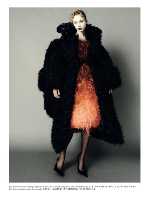 Fashion editorial shot of a woman wearing a degradé feather dress with a large black furry coat and black high heel shoes in studio.
