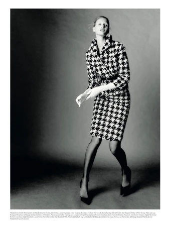 Fashion editorial shot of a model in a houndstooth skirt suit, black stockings and pumps, against a neutral backdrop in a photo studio.