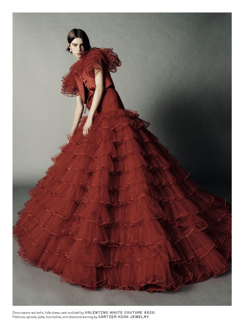 Editorial fashion photo of a woman wearing a red tiered tulle gown, captured indoors in a studio with soft, diffused lighting.