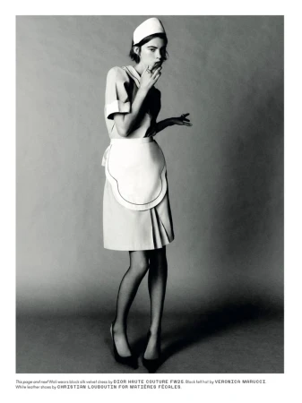Model in maid-style uniform wearing a small pillbox hat against a grey seamless studio backdrop