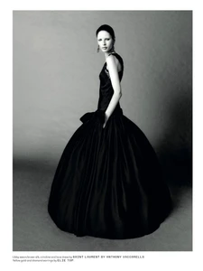 Model wearing a voluminous dark ball gown standing against a plain grey studio backdrop