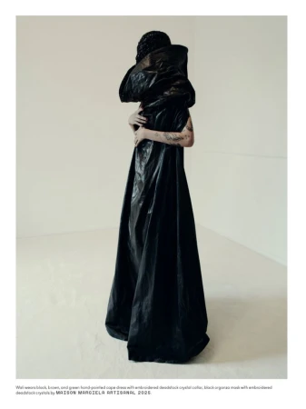 Model wearing a voluminous dark cape dress standing against a plain white studio background.