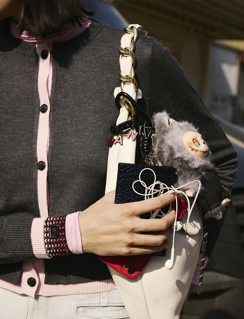 Woman poses outdoors with a white purse, showcasing a grey buttoned cardigan, a black cardholder, a phone, and a stuffed animal.
