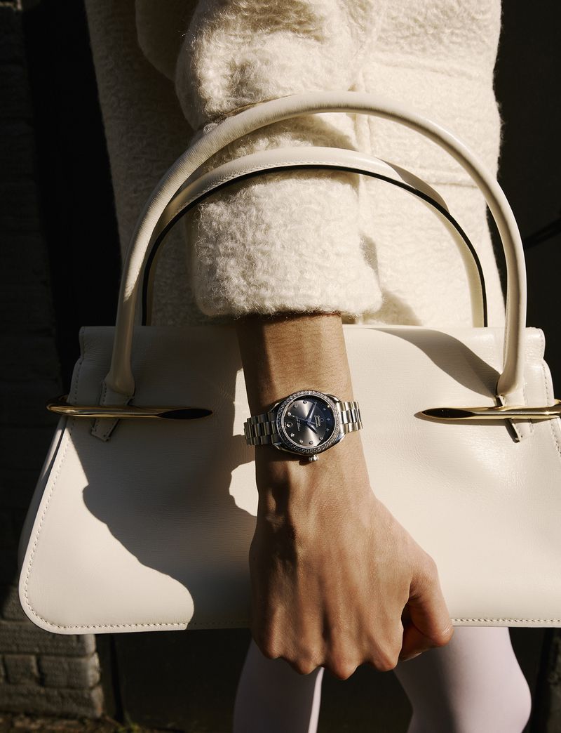 Close-up of a model wearing a silver watch and holding a structured white leather handbag for Grazia UK