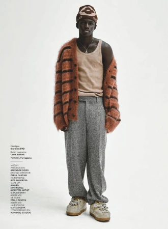 Male model wears a brown striped cardigan, tan tank top, gray tweed trousers, and sneakers in a full-length fashion studio shot.
