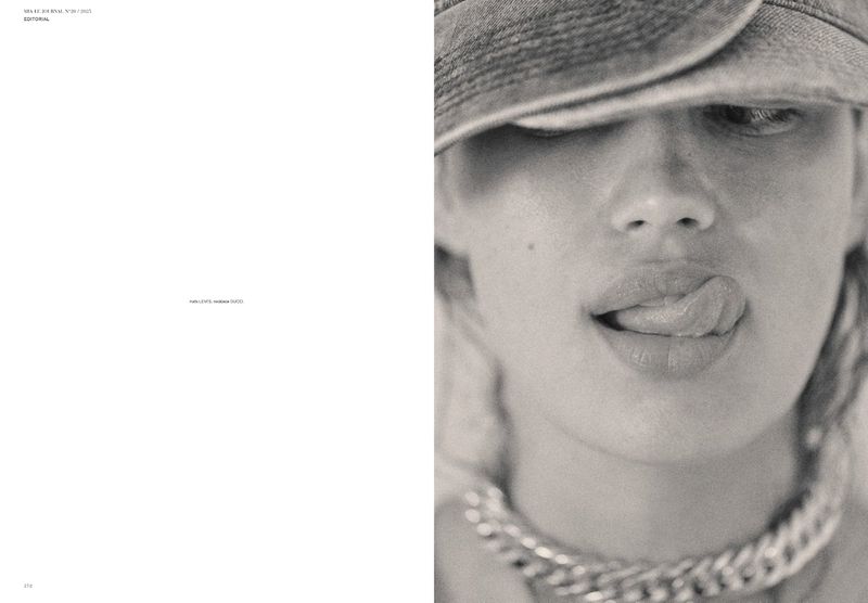Close-up portrait of a woman with a hat, sticking her tongue out, and wearing a large chain necklace in a studio.