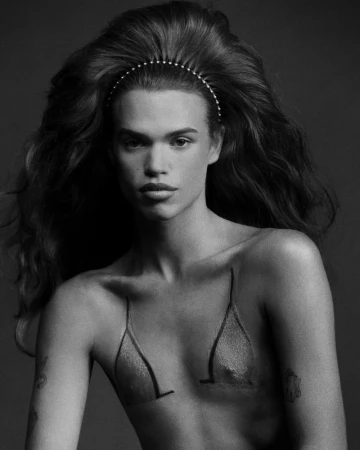 Striking black and white portrait of a person with flowing hair and body art, set against a dark grey backdrop in a photo studio.