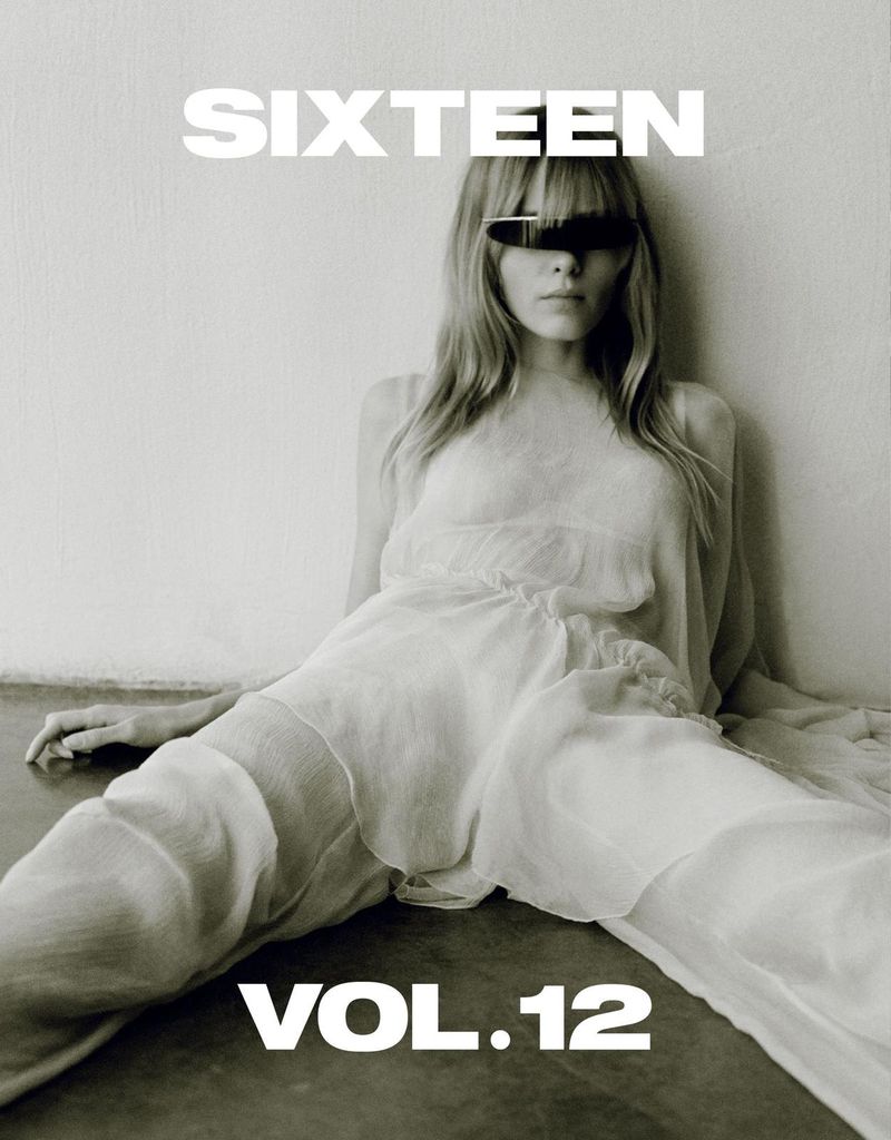 Blonde female model poses indoors wearing sunglasses and a white flowing dress against a textured wall for a fashion editorial.