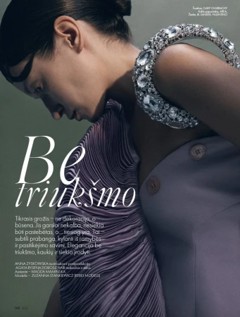 Fashion editorial shot of a woman with dark hair wearing a large, jeweled collar necklace and draped lilac fabric over her shoulder.