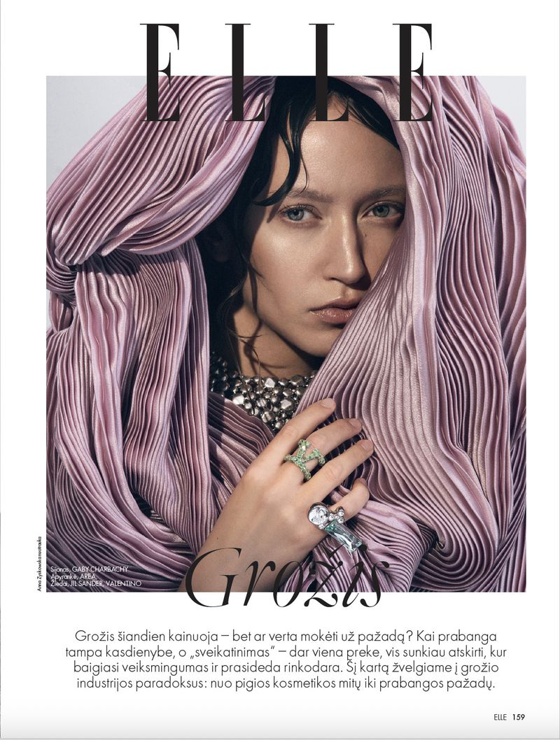 Elle magazine cover featuring a young woman with pale skin, adorned in an iridescent pink pleated dress, jewelry, and a neutral background.