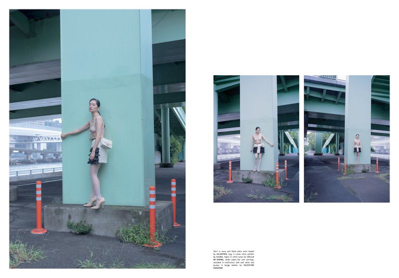 Fashion editorial shot: A woman poses under a bridge wearing a light-colored outfit and high heels, complemented by a shoulder bag.