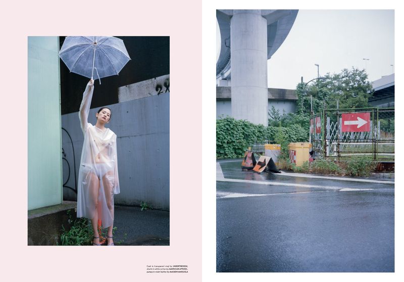 Fashion shot of an Asian woman in a transparent raincoat holding an umbrella, with an urban setting and a road scene in the background.