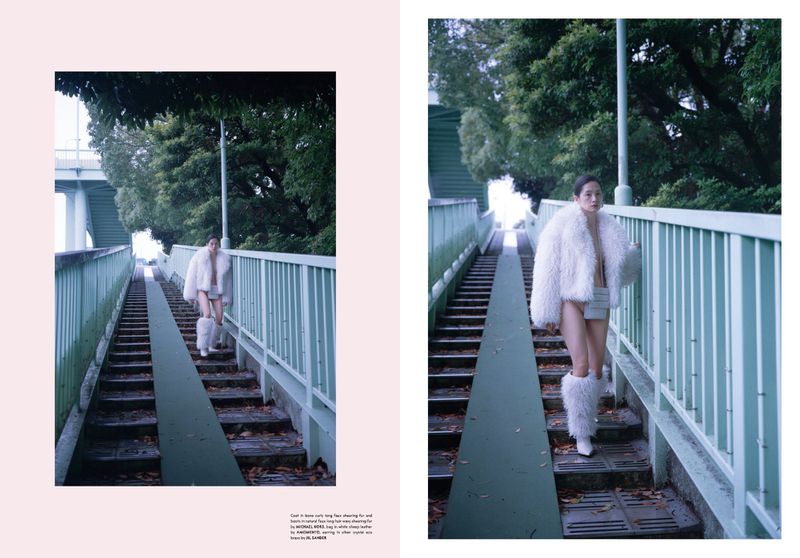 A woman with dark hair wearing a white furry jacket and shorts walks down green concrete stairs in an urban outdoor environment.