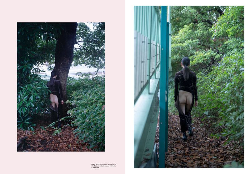 Woman in sheer black dress walks away on woodland trail, captured in two-page editorial layout with pastel background, trees and greenery.