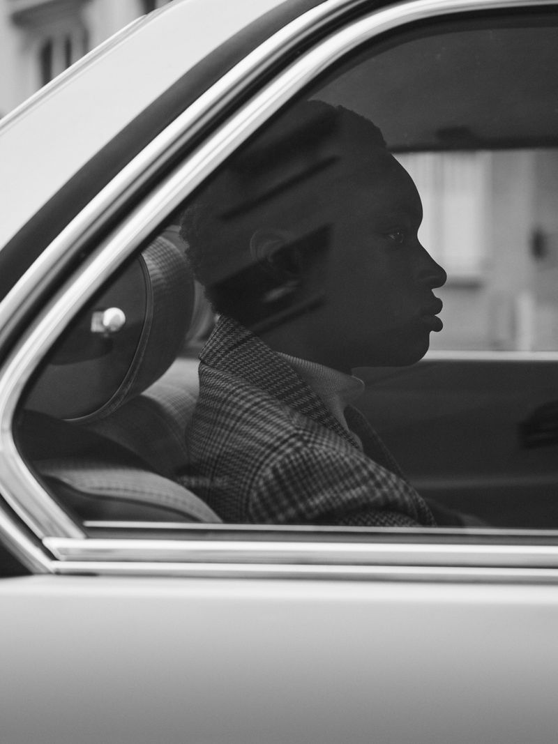 Black and white portrait of a young adult in a car, showcasing a profile view through the car window, highlighting the person's features.