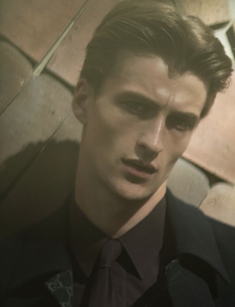 Headshot of a dark-haired adult male wearing a collared shirt and suit jacket, posing indoors against a textured background in soft lighting.