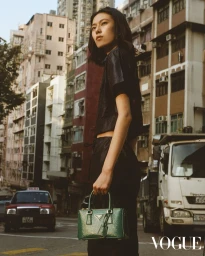 Model Puze Liu in black outfit holding a green handbag on an urban street for Vogue Hong Kong.
