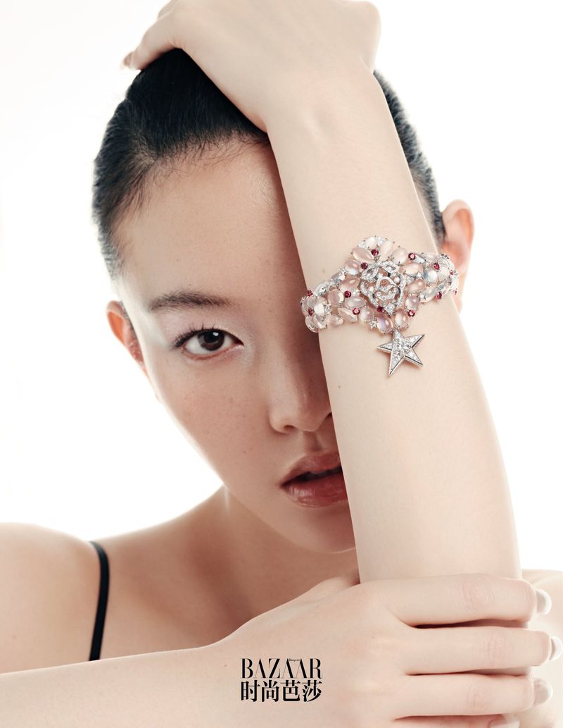Close-up fashion shot of an Asian woman wearing a floral bracelet with a star charm, fair skin, dark hair, makeup, in a studio setting.