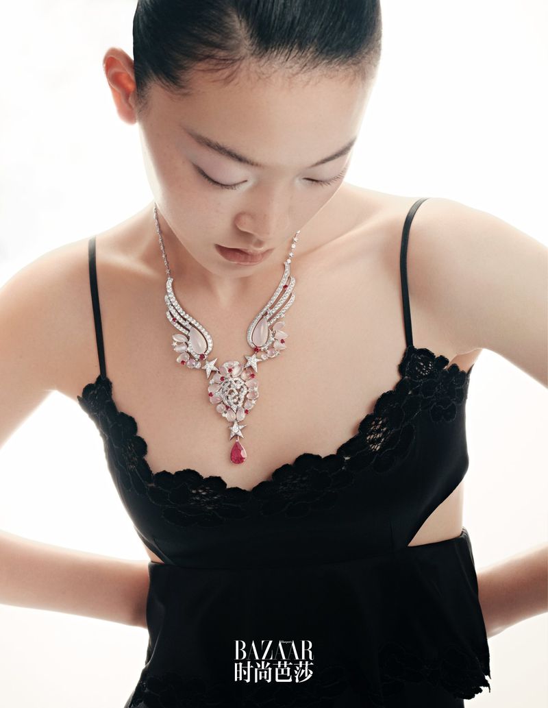 Portrait of a young woman with a dramatic necklace, wearing a black dress, shot on bright background with soft studio lighting.