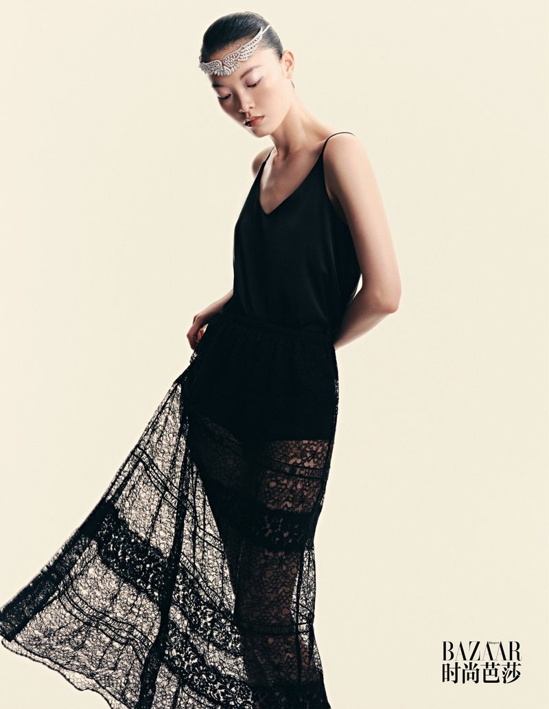 Elegant Asian woman poses in black dress and jeweled headband against a soft background in a fashion editorial style portrait.