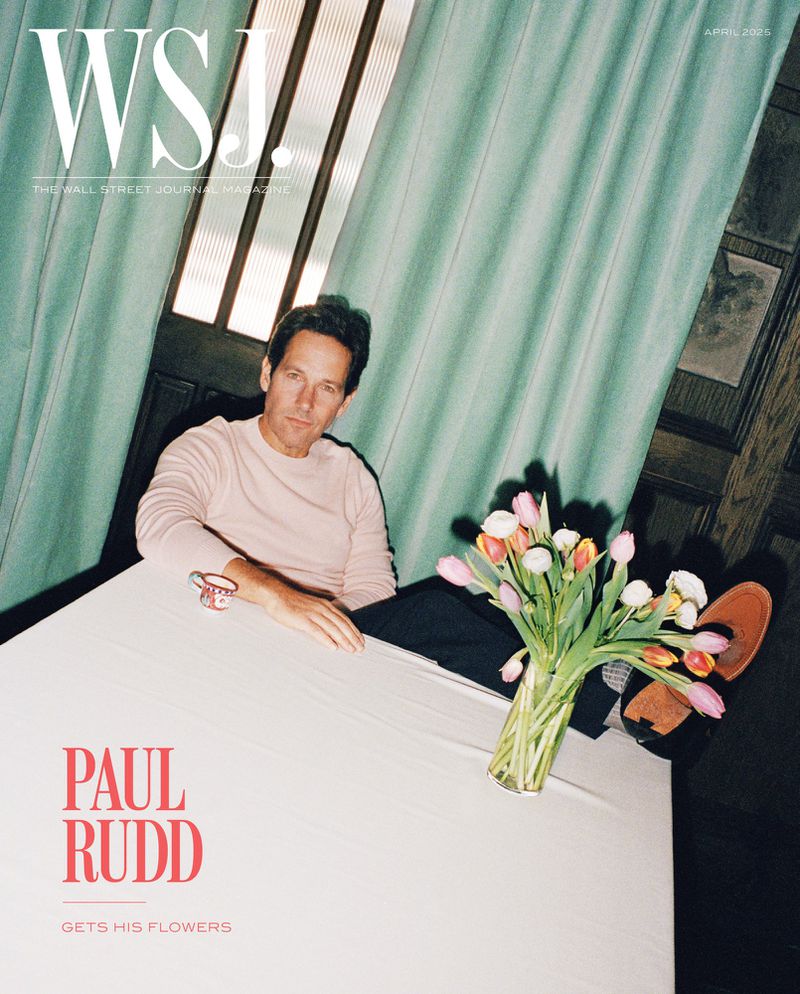 Paul Rudd sits at a table with a vase of tulips in a magazine cover shot; mint curtains and warm lighting create a classic aesthetic.