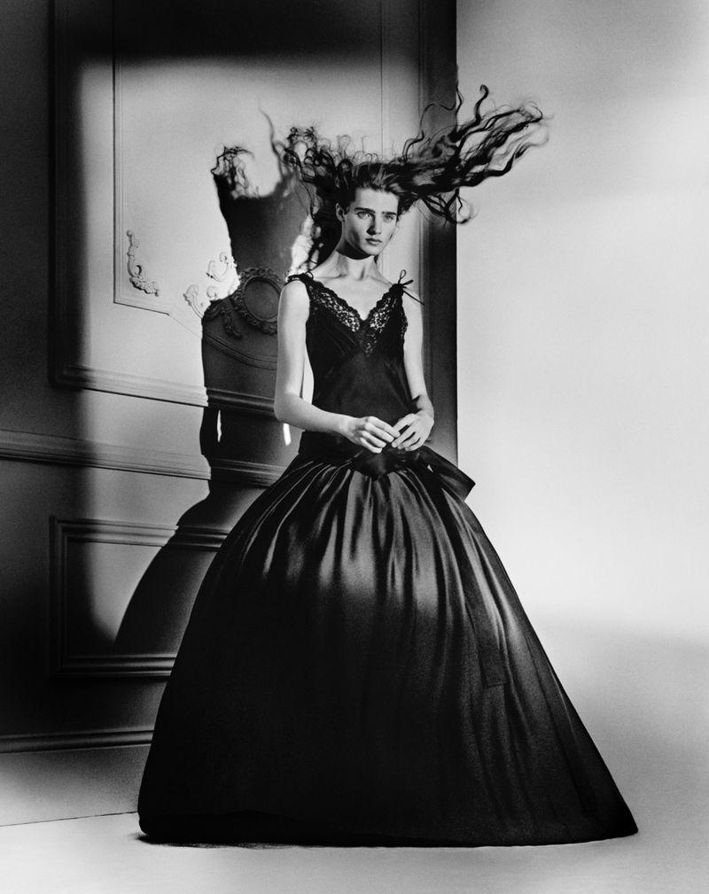 Monochrome fashion shot of a woman in a formal gown with dramatic flowing hair standing in front of a paneled wall.