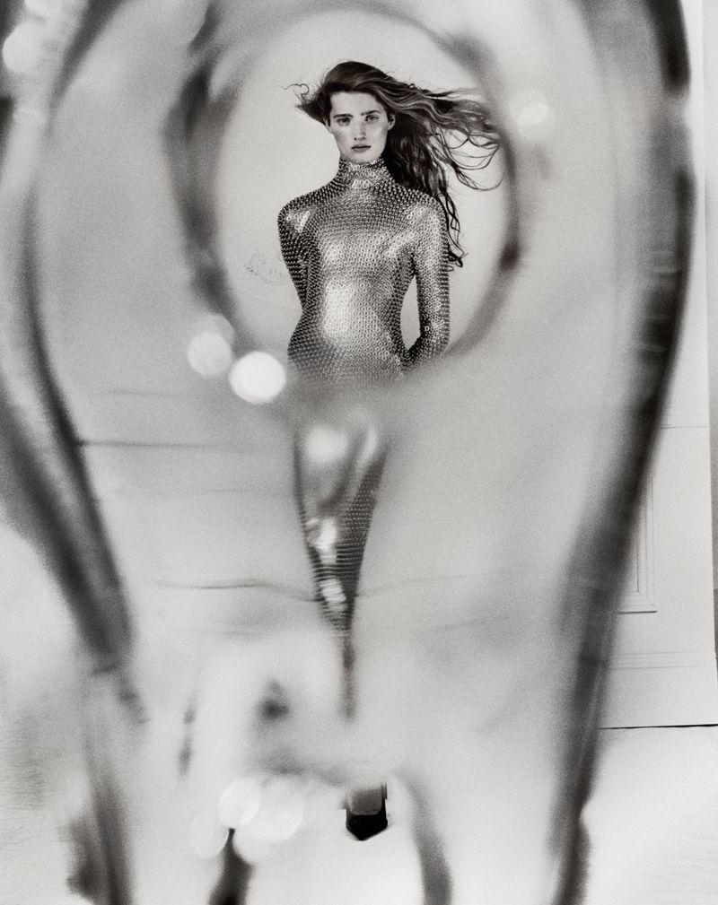 Black and white fashion shot of a woman in a metallic dress, seen through a blurred, glass-like abstract foreground.
