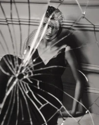 Model in a black slip dress and netted veil viewed through cracked shattered glass for Vogue Adria