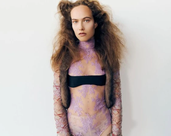 A woman with curly hair poses in a lace bodysuit with a black bandeau, against a white background. Beauty and fashion photography.