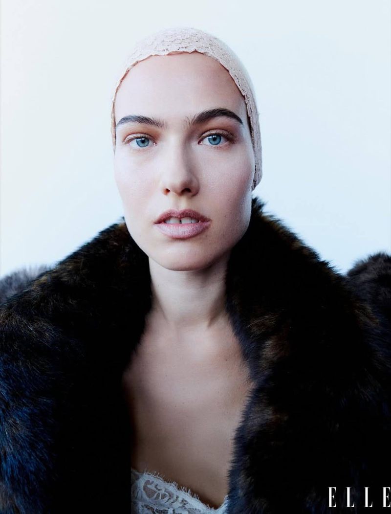 Close-up studio shot of a woman in a fur coat and lacy head covering against a white backdrop. Elle logo visible.