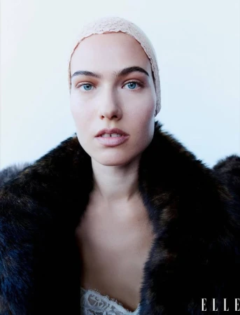 Close-up studio shot of a woman in a fur coat and lacy head covering against a white backdrop. Elle logo visible.