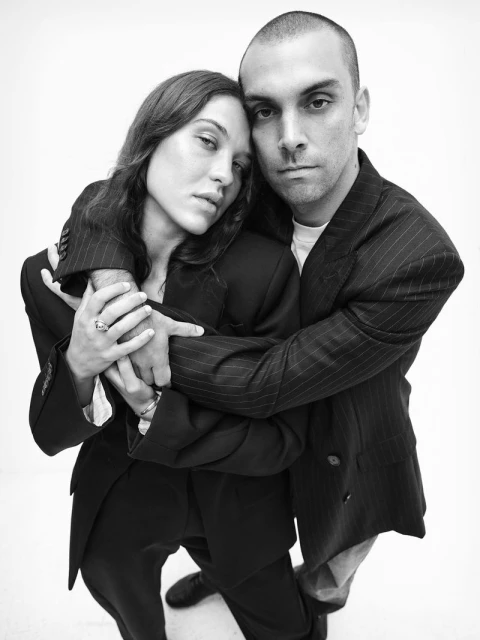 Monochrome portrait of a couple wearing suit jackets, embracing each other against a stark white background in a photo studio.
