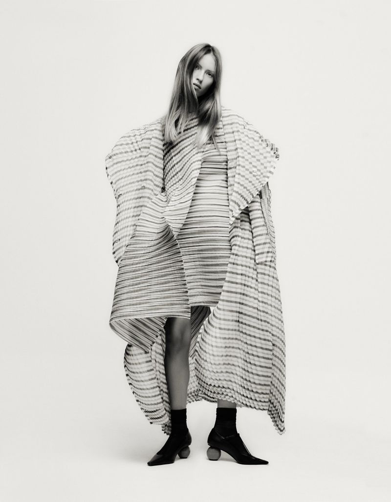 Model Lea Seelenmeyer standing against a plain white background wearing a striped patterned outfit and black shoes.