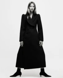 Model Lea Seelenmeyer wearing a long black coat and kitten heels against a white background for Yo Dona Spain.