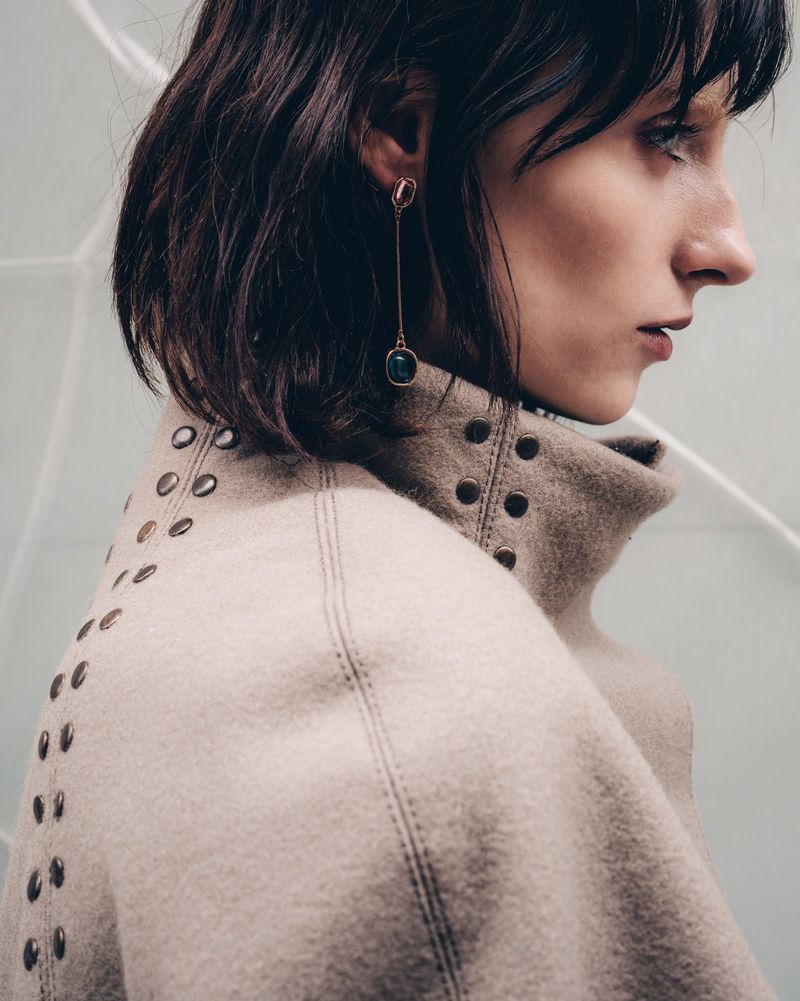 Close-up profile of a model wearing a studded beige high-neck garment and a long drop earring.