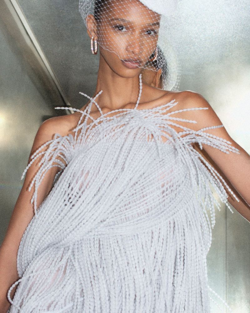 Elegant woman wearing a beaded dress and a veiled hat. Close-up shot in an indoor setting. Fashion editorial with style and grace.