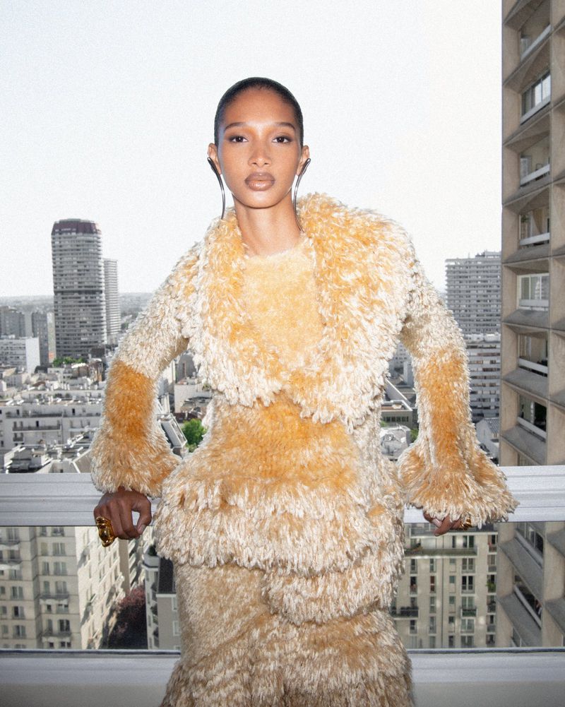 Elegant adult female poses in a shaggy, layered dress with a matching jacket in an urban setting with tall buildings in the background.