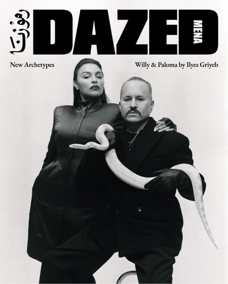 Black and white fashion editorial shot of a man and woman posing with a snake in front of a white background for Dazed magazine.