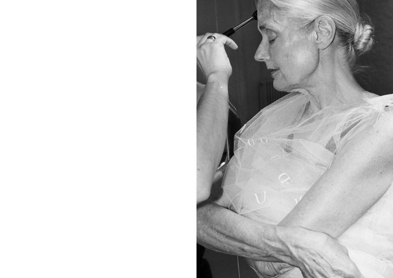 Woman receiving makeup application from makeup artist in black and white, wearing sheer fabric, hair in bun. Beauty and fashion concept.