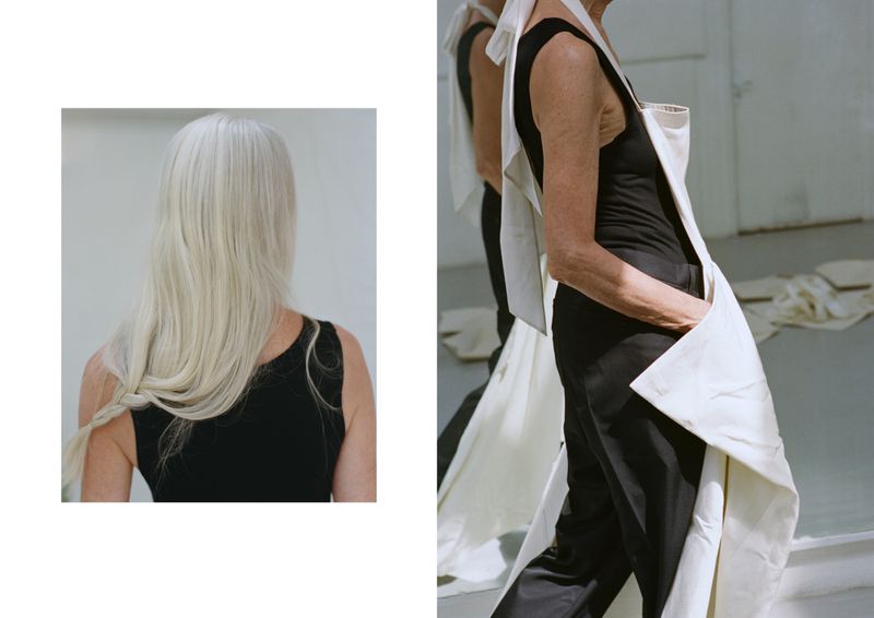 An adult woman with long, gray hair and a black tank top is seen from the back, while another woman wears a white apron-like garment.