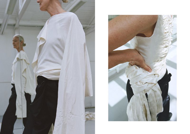 Elegant older woman in draped cream top and black pants, reflected in a mirror, next to a torso wearing a similar draped cream top.