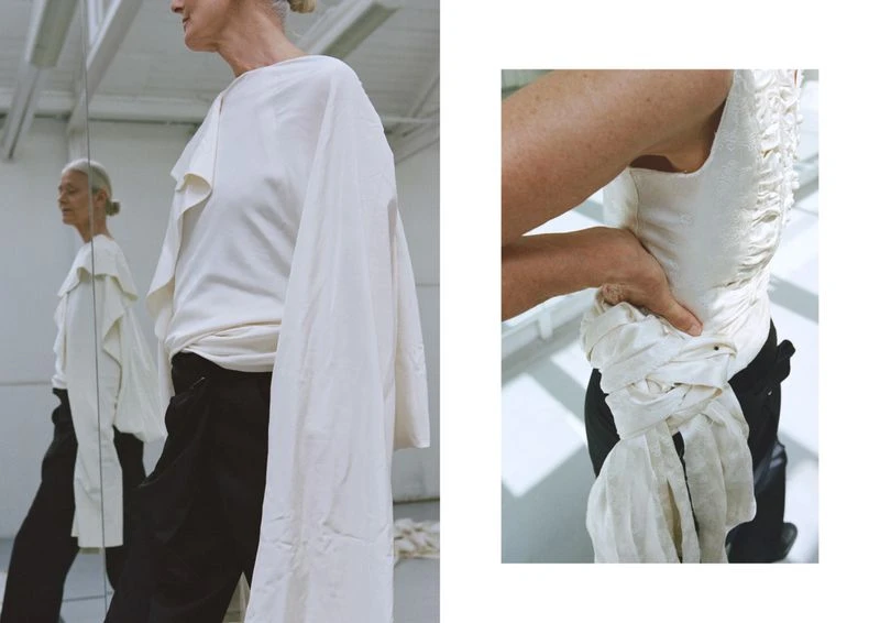 Elegant older woman in draped cream top and black pants, reflected in a mirror, next to a torso wearing a similar draped cream top.