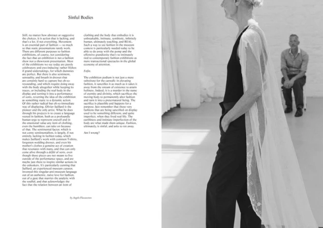 Older model stands in black outfit with sheer veil; older man in background on chair. Black and white fashion editorial shot.